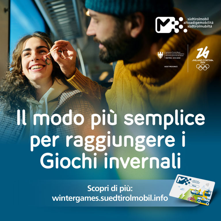 Giovane donna sorridente mentre le vengono dipinti gli anelli olimpici sul viso. Testo nell’immagine: ‘Il modo più semplice per raggiungere i Giochi Invernali’, con riferimento a wintergames.suedtirolmobil.info e i loghi di altoadigemobilità, Provincia autonoma di Bolzano e Milano Cortina 2026.